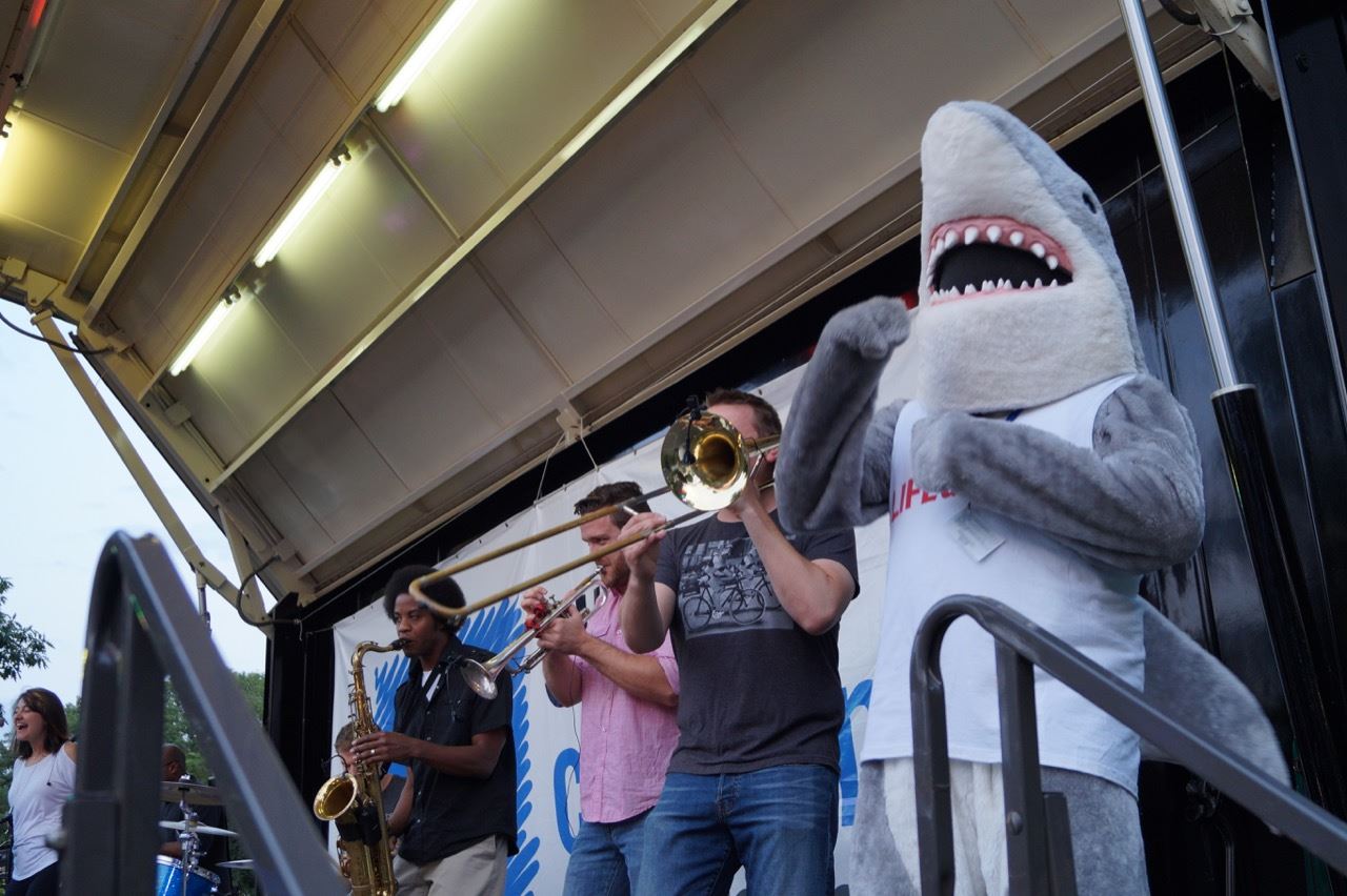 Shark mascot plays the air trombone with members of the band.